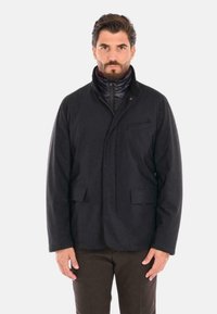 Giacca nera leggera con chiusura frontale a zip, colletto ripiegabile, due tasche frontali e una texture di tessuto liscia.