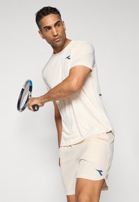 Light beige athletic shirt and shorts, featuring a blue logo. The shirt has short sleeves and relaxed fit, suitable for sports activities.