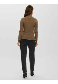 Hellbrauner Rollkragenpullover, figurbetontes Design, gerippte Bündchen und Saum; kombiniert mit dunklen Jeans und schwarzen Stiefeletten, von hinten betrachtet.