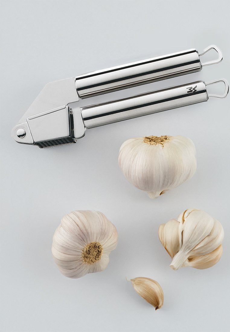 Knoblauchpresse aus Edelstahl mit einer strukturierten Riebenfläche; beinhaltet drei Knoblauchzehen, eine davon in Zehen getrennt, auf einem hellen Hintergrund.