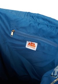 Interno in tessuto blu di una borsa con una tasca con zip e un'etichetta bianca con un logo del sole arancione, che indica il marchio "SUNDEK."