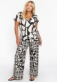 Haut à motifs noir et crème avec des manches courtes et un col en V, associé à un pantalon large avec un design graphique audacieux contrastant.