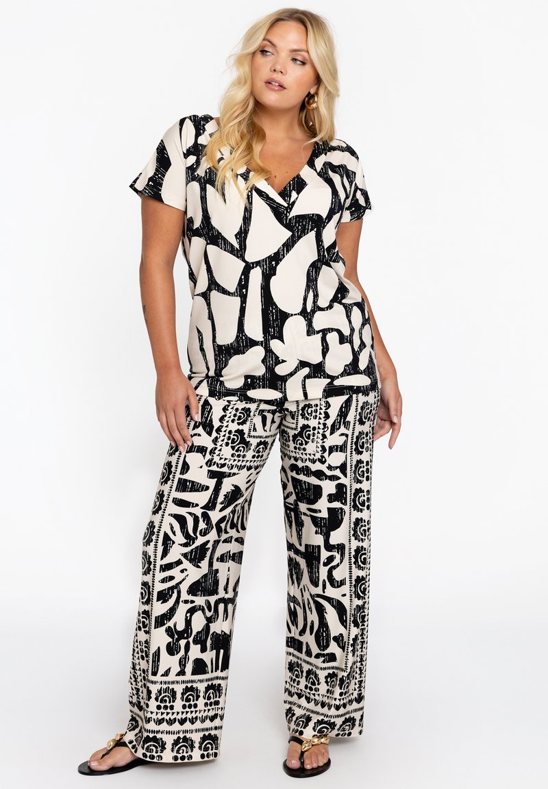 Haut à motifs noir et crème avec des manches courtes et un col en V, associé à un pantalon large avec un design graphique audacieux contrastant.