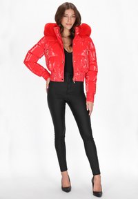 Czerwona, błyszcząca kurtka puchowa z kapturem wykończonym sztucznym futrem, krótki fason, zapinana na zamek, z prążkowanymi mankietami, zestawiona z obcisłymi czarnymi spodniami i szpilkami.