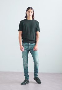 Schwarzes kurzärmliges T-Shirt, hellblaue Slim-Fit-Jeans, schwarze Sneaker. Glatte Textur, enganliegendes Design, steht vor einem schlichten Hintergrund.