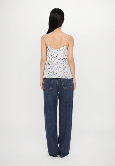Floral print camisole with thin straps in light cream and blue; paired with loose, dark blue denim pants with a straight leg and pockets.