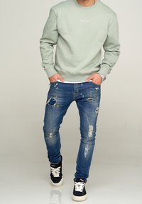 Jasnozielona bluza z okrągłym dekoltem, zestawiona z wyblakłymi niebieskimi dżinsami z przetarciami i plamami farby; czarno-białe trampki.