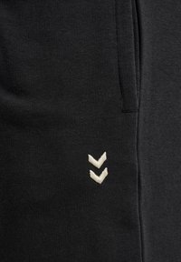 Gros plan sur un tissu noir avec deux bandes blanches en forme de chevrons et une couture, probablement une partie de la zone de poche d'un vêtement.