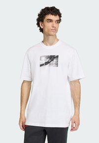 Λευκό βαμβακερό T-shirt με κοντά μανίκια, με ασπρόμαυρο γραφικό σχέδιο χειρός και αθλητικού παπουτσιού στην μπροστινή πλευρά. Χαλαρή εφαρμογή.