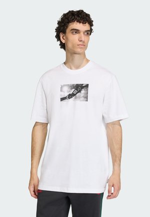 Λευκό βαμβακερό T-shirt με κοντά μανίκια, με ασπρόμαυρο γραφικό σχέδιο χειρός και αθλητικού παπουτσιού στην μπροστινή πλευρά. Χαλαρή εφαρμογή.