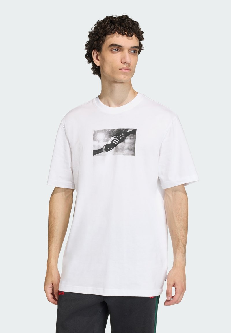 Λευκό βαμβακερό T-shirt με κοντά μανίκια, με ασπρόμαυρο γραφικό σχέδιο χειρός και αθλητικού παπουτσιού στην μπροστινή πλευρά. Χαλαρή εφαρμογή.