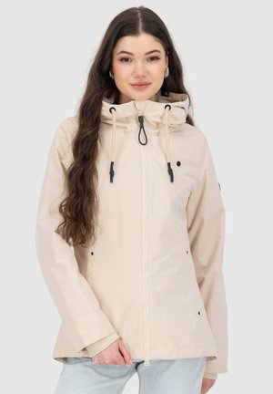 Giacca impermeabile beige chiaro con cappuccio, zip frontale e cordoncino. Presenta dettagli neri e tasche a mano. Texture liscia.