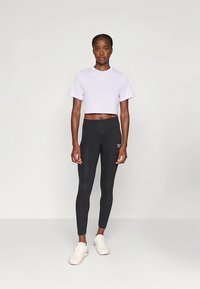 Orezaná levanduľová tričko v kombinácii s čiernymi legínami a bielymi teniskami. Legíny majú hladkú textúru, priliehavý strih a detail s logom.