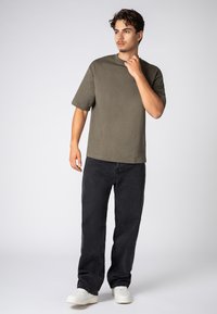Olive green short-sleeve t-shirt, loose fit, paired with black denim jeans and white sneakers. Simple design with no visible patterns.