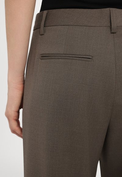 Un pantalon brun ajusté avec une texture lisse, doté d'une poche arrière et de passants de ceinture, présenté de côté.