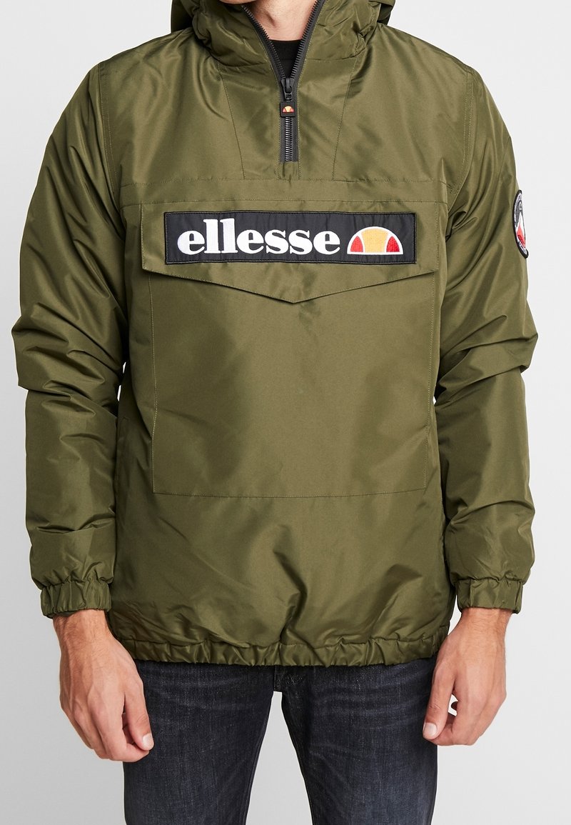 Olivengrøn pullover-jakke lavet af nylon med en forlomme, sort logoemblem og elastiske manchetter samt kant. Hættedesign.