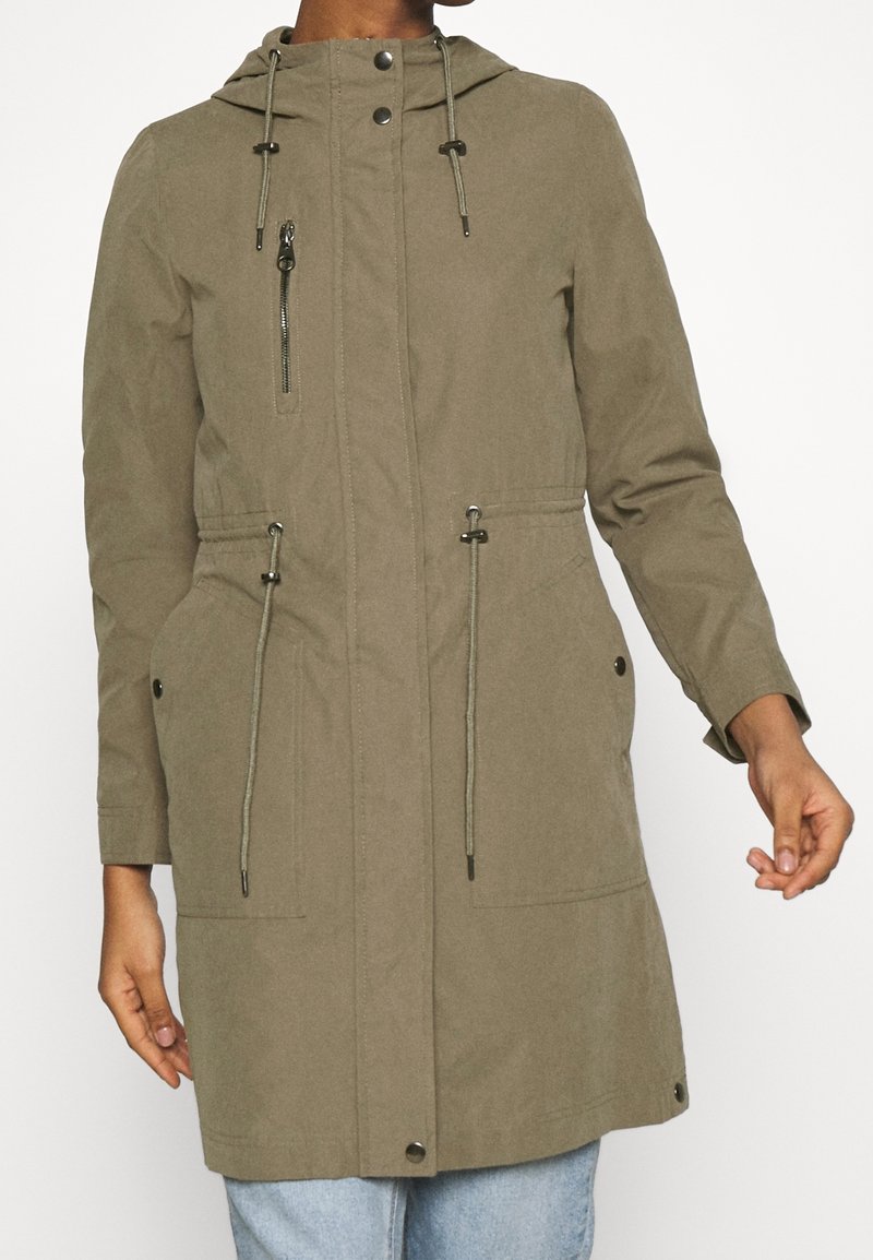 Olivově zelená parka s kapucí, nastavitelné šňůrky, přední zip a patentní knoflíky, a boční kapsy. Hladká textura a délka do pasu.