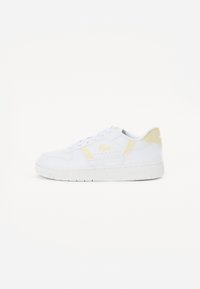 Fehér sneaker sárga részletekkel, sima bőrből készült. Lekerekített orra, fűzős kialakítása és márkafeliratok találhatók az oldalon és a saroknál.