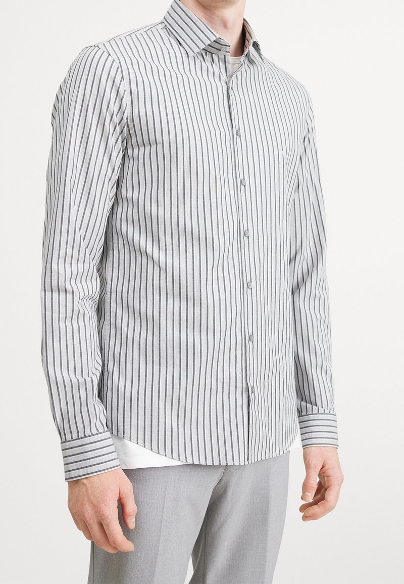 Grå og hvide stribede skjorte med knapper, klassisk krave, lange ærmer og buet kant. Materialet virker som bomuld med en tekstur af lodrette linjer.