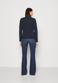 Maglietta a maniche lunghe blu navy con colletto alto, abbinata a jeans svasati blu scuro. I jeans hanno tasche posteriori e una leggera sbiaditura.