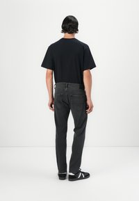 Black short-sleeve shirt, gray jeans, and black sneakers viewed from the back. Simple design with a relaxed fit, clean lines, and no visible logos.
