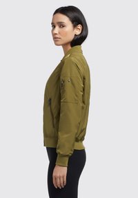 Olive roheline bomber-jakk sileda viimistlusega, millel on soonikud mansettide ja äärte juures, lukuga taskud ning detailne õmblusvarustus varrukatel.