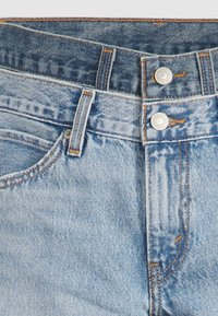 Jeans de denim en tonos azul claro y oscuro apilados, mostrando las cinturas, los lazos para el cinturón, los botones y las costuras detalladas.