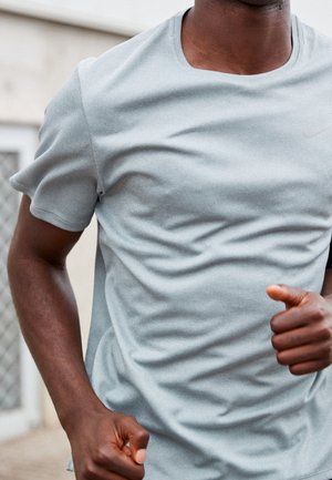 Mann in hellgrauem Sportshirt joggt draußen mit angewinkelten Armen und geballten Fäusten, Oberkörper und Oberarme sichtbar.