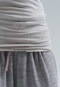 Ljust färgad åtsittande topp med skräddarsydd midja, kombinerad med en grå plisserad nederdel. Tyget verkar mjukt och något texturerat. Rosa dragsko-detalj synlig.