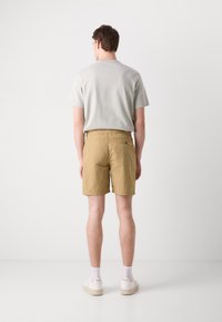 Pantaloni scurți khaki cu o finisare texturată, talie elastică și un buzunar pe spate. Asortați cu un tricou cu mânecă scurtă de culoare gri deschis și adidași albi.