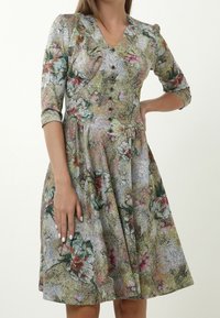 Blumenmusterkleid mit V-Ausschnitt, Knopfverschluss vorne, Ballonärmeln und ausgestellt Rock. Die Farben umfassen Grün, Pink und Beige.