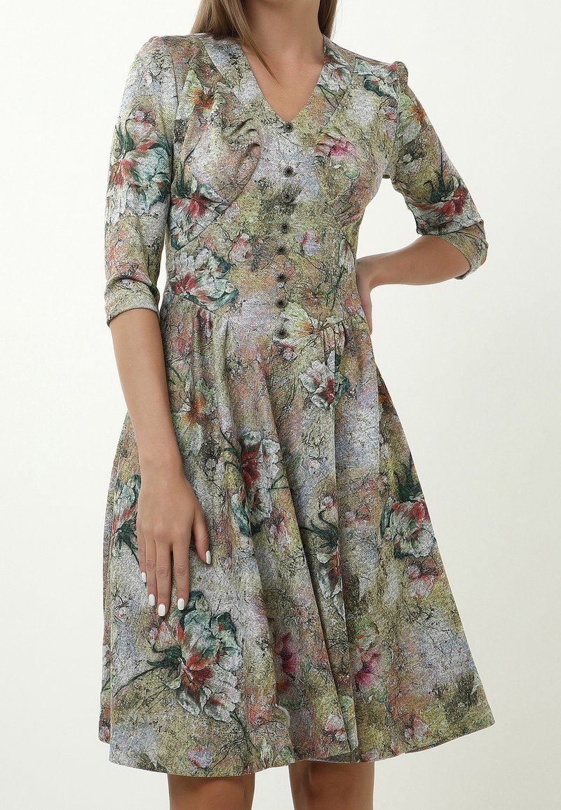 Blumenmusterkleid mit V-Ausschnitt, Knopfverschluss vorne, Ballonärmeln und ausgestellt Rock. Die Farben umfassen Grün, Pink und Beige.