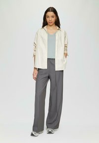 Gestreiftes beiges Button-Up-Hemd über einem hellblauen V-Ausschnitt-Top, kombiniert mit grauen weiten Hosen und silbernen Sportschuhen.