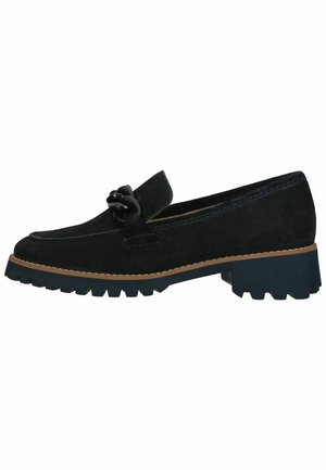 Mocassin en suédine noire avec un nœud décoratif, semelle en caoutchouc et coutures beige contrastantes. Talon bas et épais avec un motif de grip texturé.