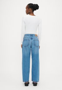 Λευκό μακρυμάνικο τοπ σε συνδυασμό με ψηλόμεσο, φαρδύ μπλε τζιν παντελόνι με δερμάτινη ετικέτα στο πίσω μέρος και κλασικό σχεδιασμό με πέντε τσέπες.