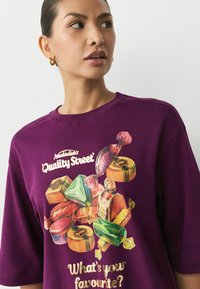 Lila Baumwoll-T-Shirt mit einem bunten Süßigkeiten-Motiv und dem Text: "Was ist dein Favorit?" Mit Rundhals- und Kurzarmdesign.
