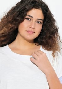 Valkoinen lyhythihainen toppi, jossa on pyöreä pääntie. Ominaisuuksina pehmeä kangas ja hienovarainen tekstuuri. Korostettuna raidallisella yksityiskohdalla hihoissa.