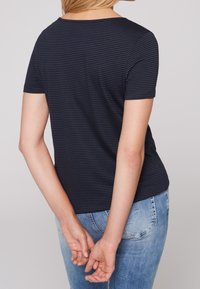 Námořnické modré pruhované tričko s krátkými rukávy, kulatým výstřihem a volným střihem, kombinované se světle modrými džíny. Měkká textilie.