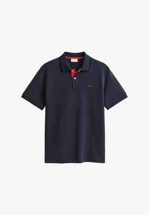 Tumši zils īsroku polo krekls ar sarkanu apkakli, divu pogu aizdari un mazu sarkanu izšūtu logotipu uz krūtīm. Mīksts kokvilnas audums.