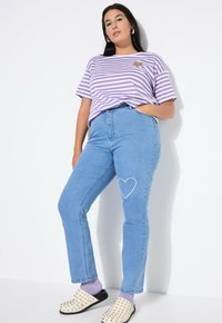 Randig lila och vit t-shirt, blå högmidjade jeans med en hjärtformad kontur på vänster knä, och nitarfärgade sandaler med lila strumpor.