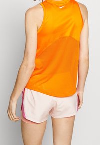 Haut sans manches Nike en orange vif avec un dos en mesh respirant ; associé à un short rose clair avec des accents roses sur les côtés.