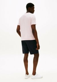 Koszulka z krótkim rękawem w blado różowym kolorze z okrągłym dekoltem, w połączeniu z ciemnonawodnymi szortami cargo i białymi sneakerami, widok z tyłu.
