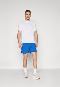 Camiseta atlética de manga corta blanca combinada con pantalones cortos azules, con tejido transpirables y un diseño ligero. Complementada con zapatillas blancas casuales.