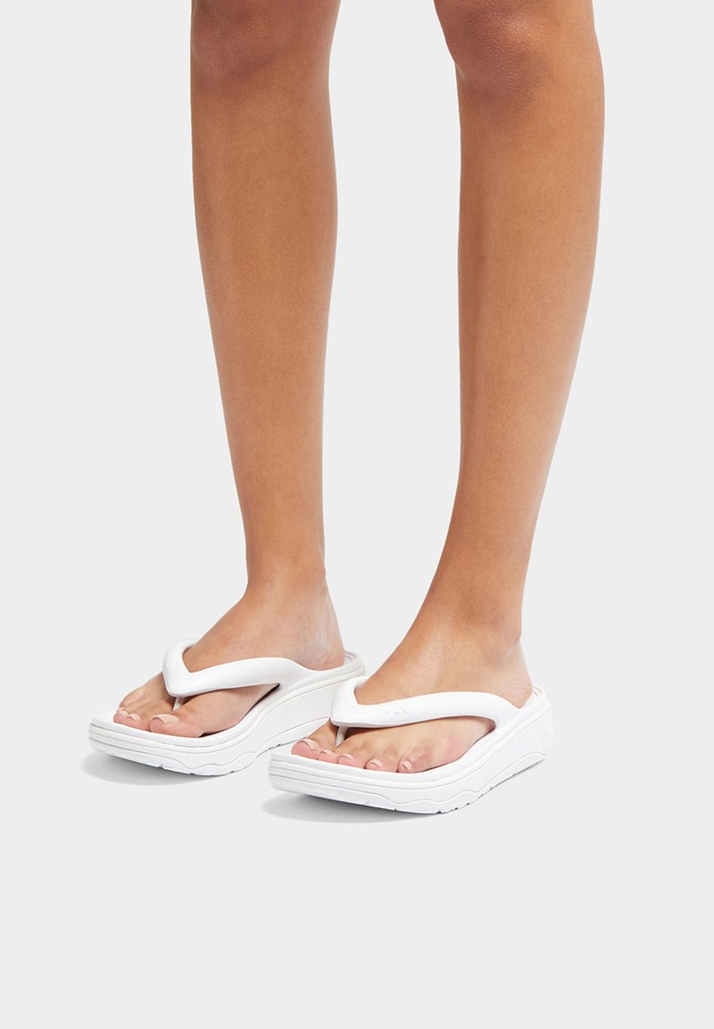 Witte flip-flopsandalen met een dikke zool, V-vormig bandontwerp, gladde textuur en een lichte kromming die de contouren van de voet accentueert.