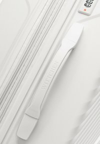 White suitcase featuring a textured surface, vertical grooves, a branded handle, and a combination lock. Smooth zipper detail visible.