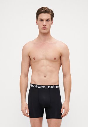 Schwarze Boxer-Shorts aus einem weichen, dehnbaren Stoff, mit einem elastischen Bund in Weiß mit Logo. Das Design sitzt eng an, ohne sichtbare Muster oder Akzente.