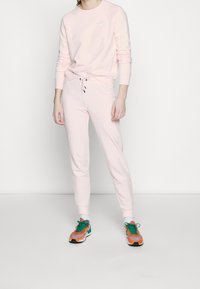 Ljusrosa sweatshirt med långa ärmar och rundad krage, ihopparad med matchande joggers som har resårmidja och dragsko.