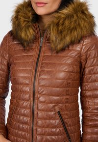 Bruine leren jas met horizontaal gestikt ontwerp, ritssluiting aan de voorkant en zijzakken. Bevat een afneembare bontkraag in een goudbruine kleur.