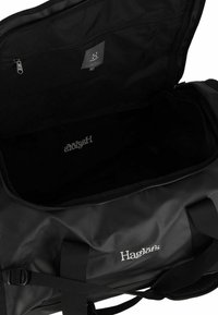 Borsa a tracolla nera realizzata in un materiale liscio e impermeabile. Presenta una grande apertura con zip, tracolle robuste e un logo ricamato all'interno.