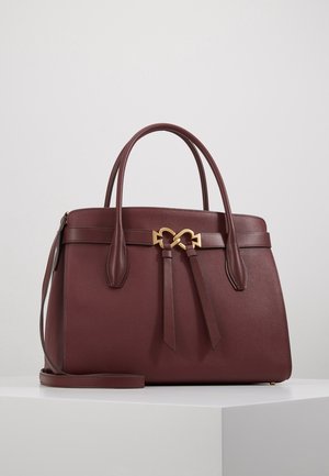 Sac à main en cuir marron foncé avec deux poignées, une bandoulière amovible et un fermoir doré en forme de cœur sur une surface blanche.